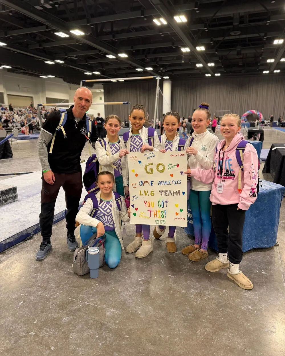 A ONE Athletics coach and team athletes holding a hand-painted sign at a meet