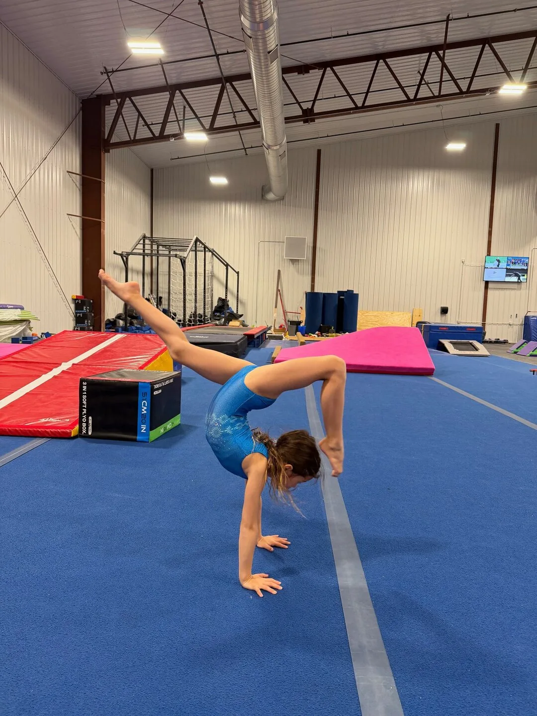 A gymnast balancing on one hand on the blue floor