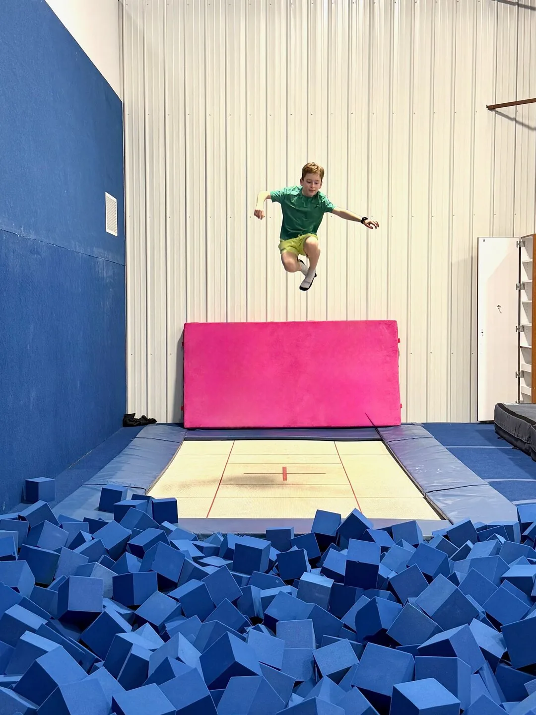 A child mid-air above the foam pit after a run down the tumbling strip