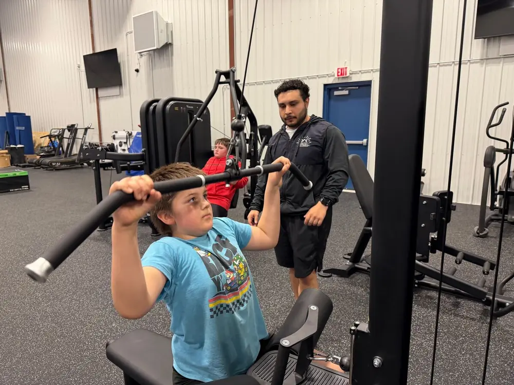 A lifter on the lat pull-down machine with a coach guiding his form