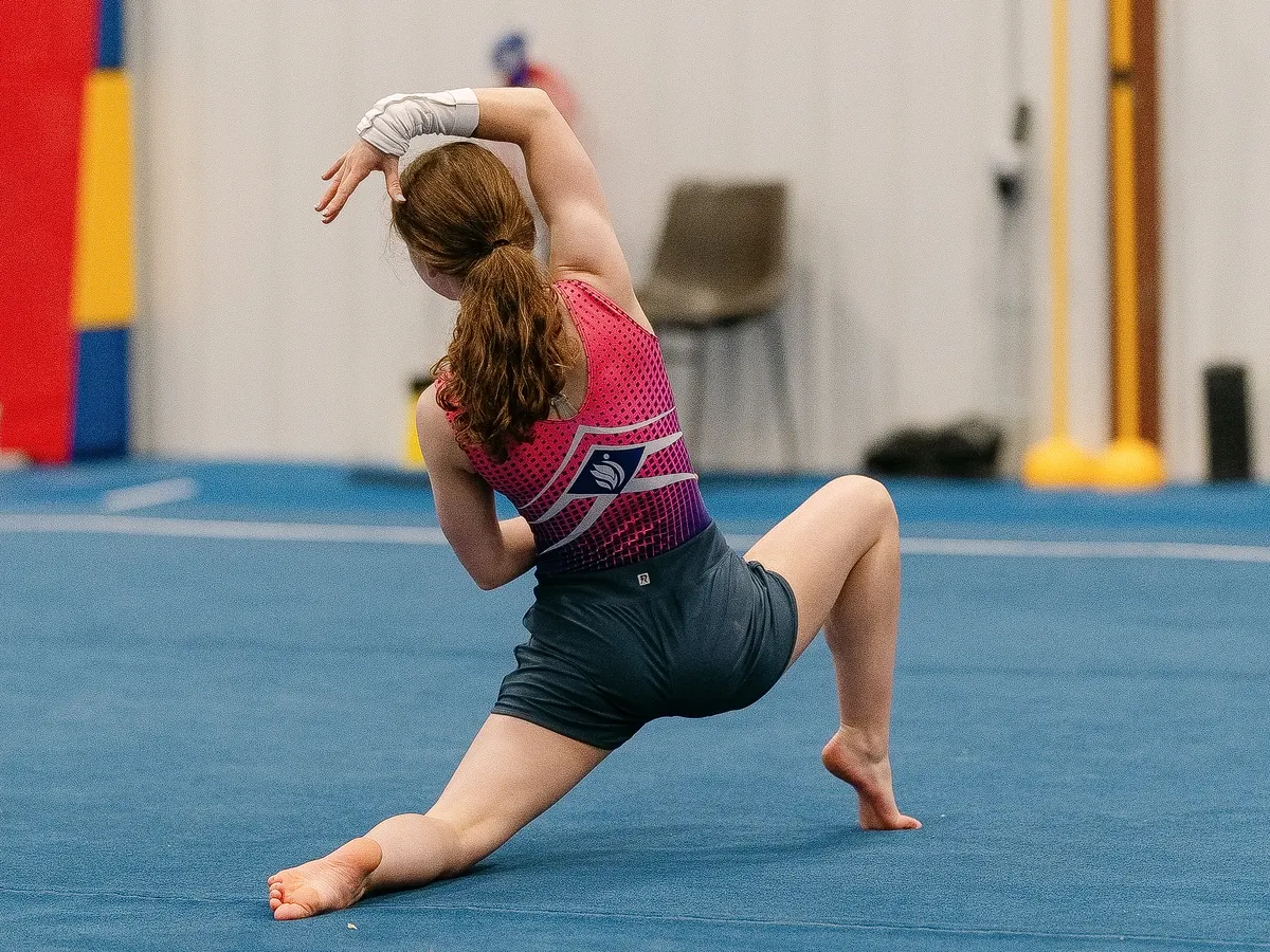 A gymnast striking a floor pose on the blue spring floor