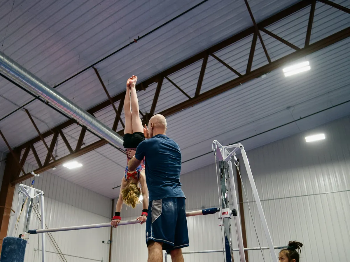 Head coach Valentin Frunzac spotting a gymnast through a handstand on the high bar